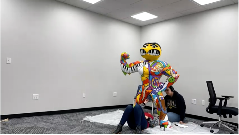Rachel Hansen lays under Herky and Sadé Head sits behind him to work on the fine line painting.